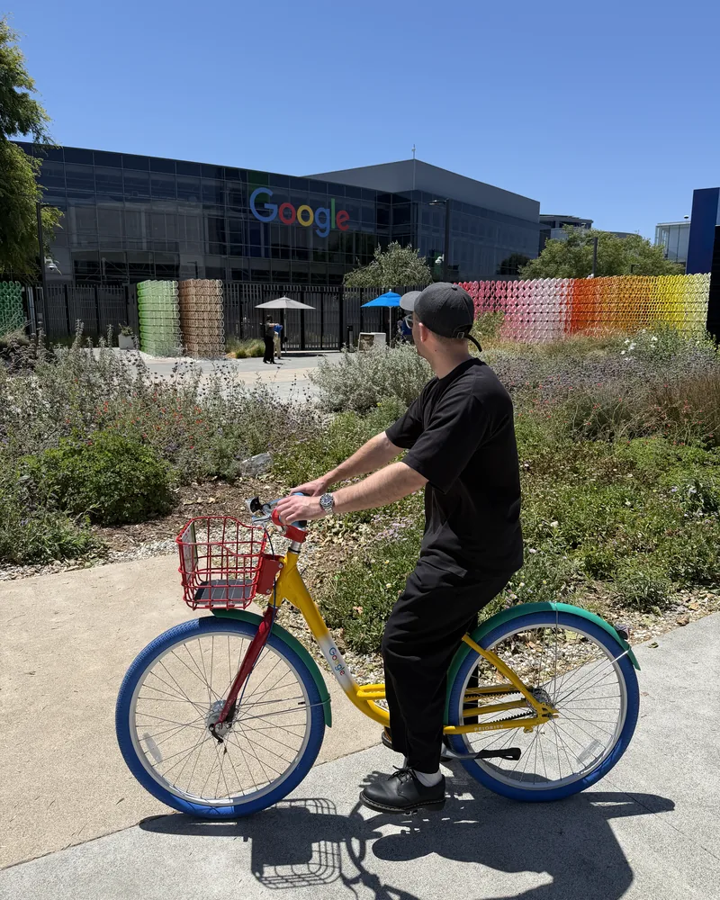 Adam Stewart riding a Google campus bicycle outside a Google building